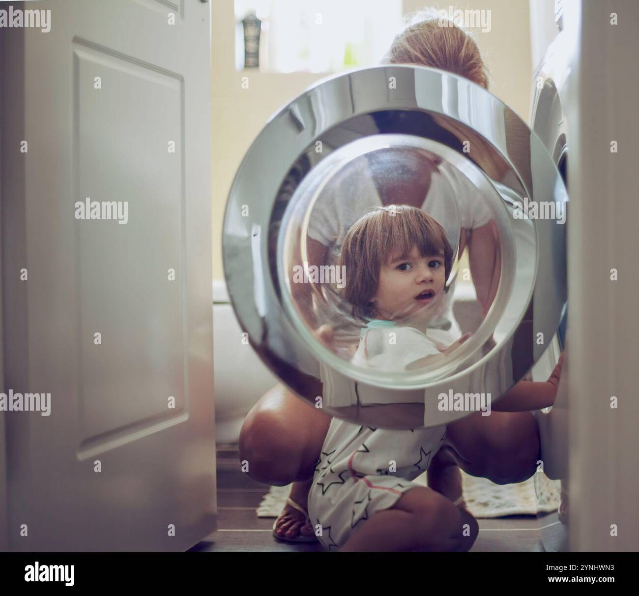 In una casa calda e invitante, una madre e il suo giovane figlio condividono un momento di legame mentre fanno il bucato. Il ragazzo guarda curiosamente attraverso il lavabo Foto Stock