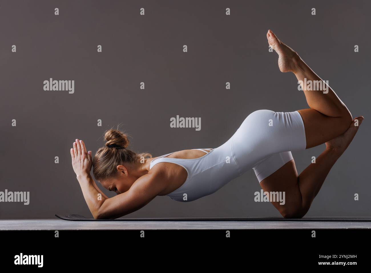 Donna adulta che esegue una posa yoga difficile su un tappetino, dimostrando flessibilità e forza. allenamento pilates, salute del corpo Foto Stock
