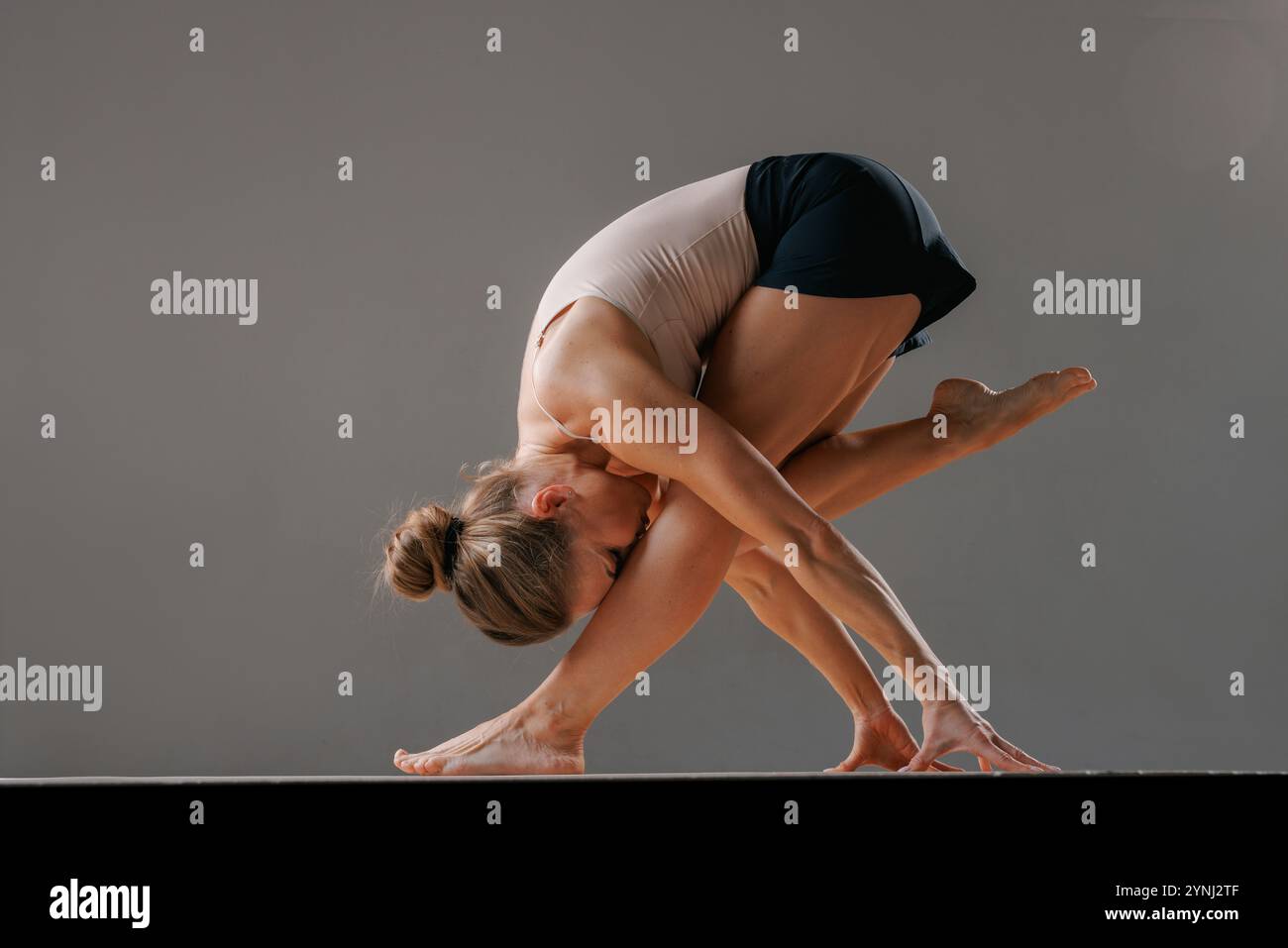 Donna adulta che esegue una posa yoga difficile su un tappetino, dimostrando flessibilità e forza. allenamento pilates, salute del corpo Foto Stock
