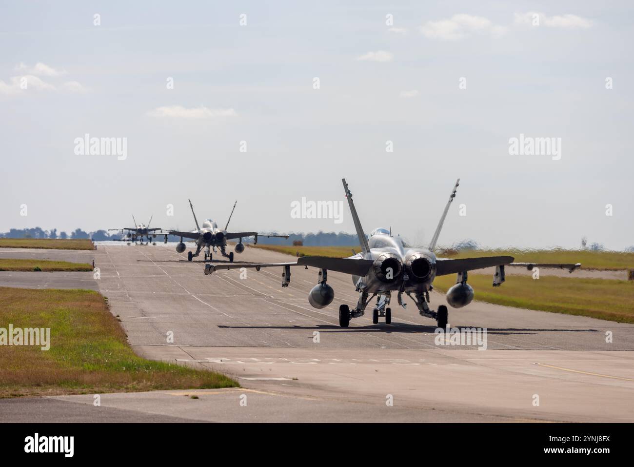 Una fila di jet da caccia scendono lungo la pista, preparandosi al decollo. Questa immagine dinamica enfatizza la precisione, il coordinamento e la prontezza di milita Foto Stock