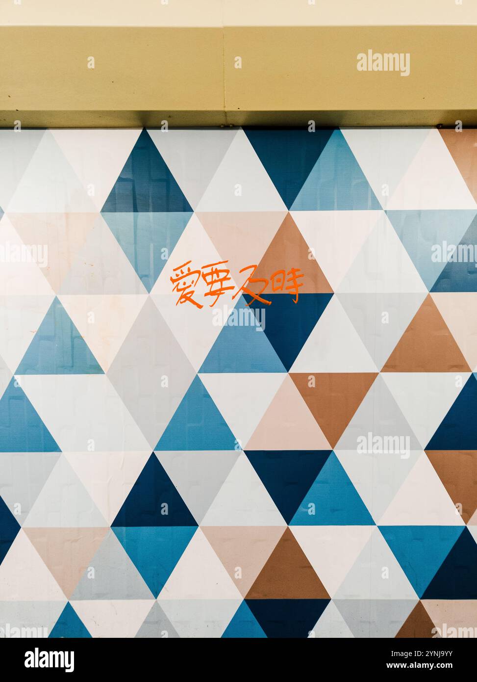 Murale geometrico con vivaci motivi triangolari e testo scritto a mano in un ambiente Urban Design Foto Stock