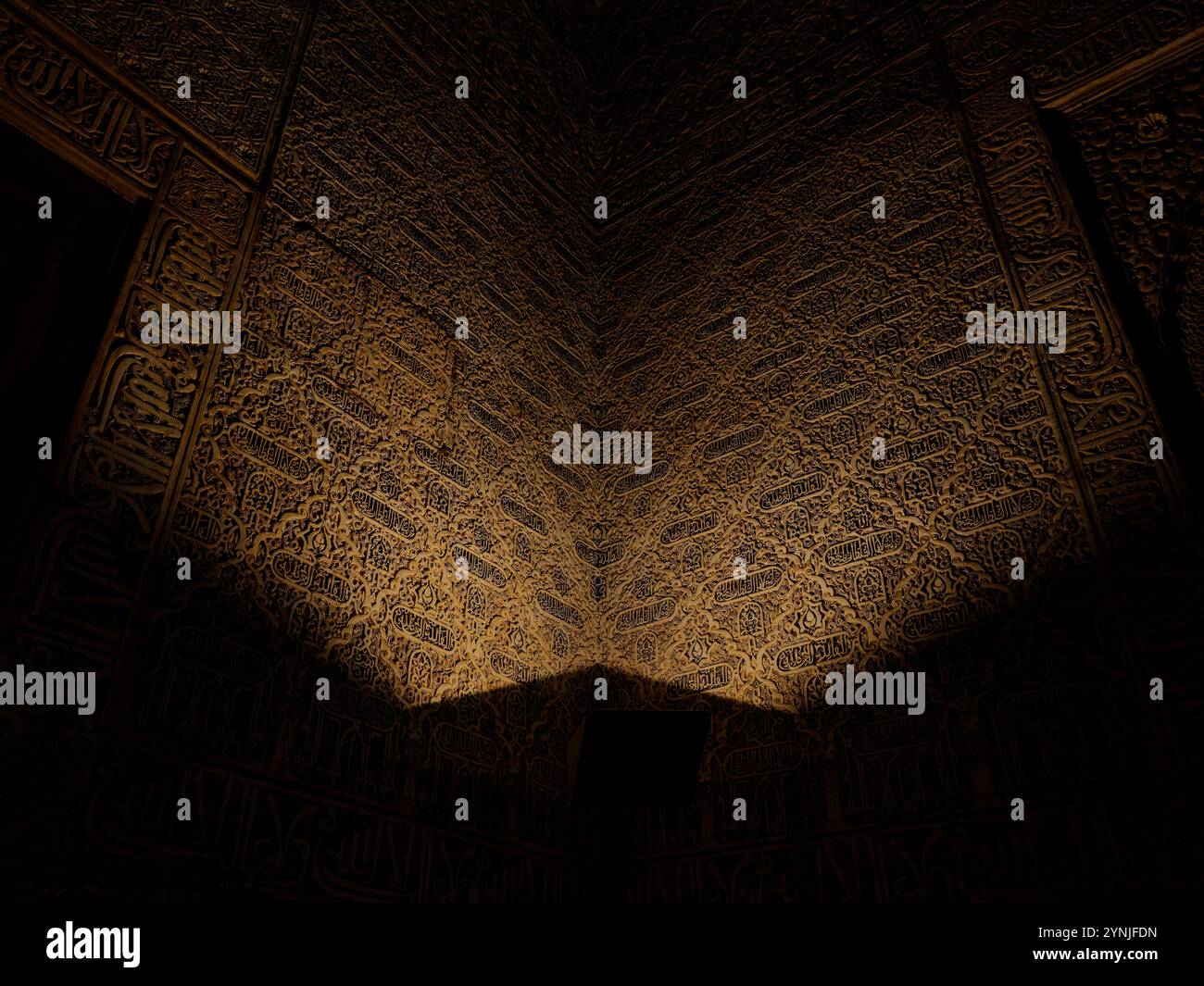 Intricata calligrafia araba illuminata da luce soffusa nei Palazzi Nasridi, Alhambra di Granada Foto Stock