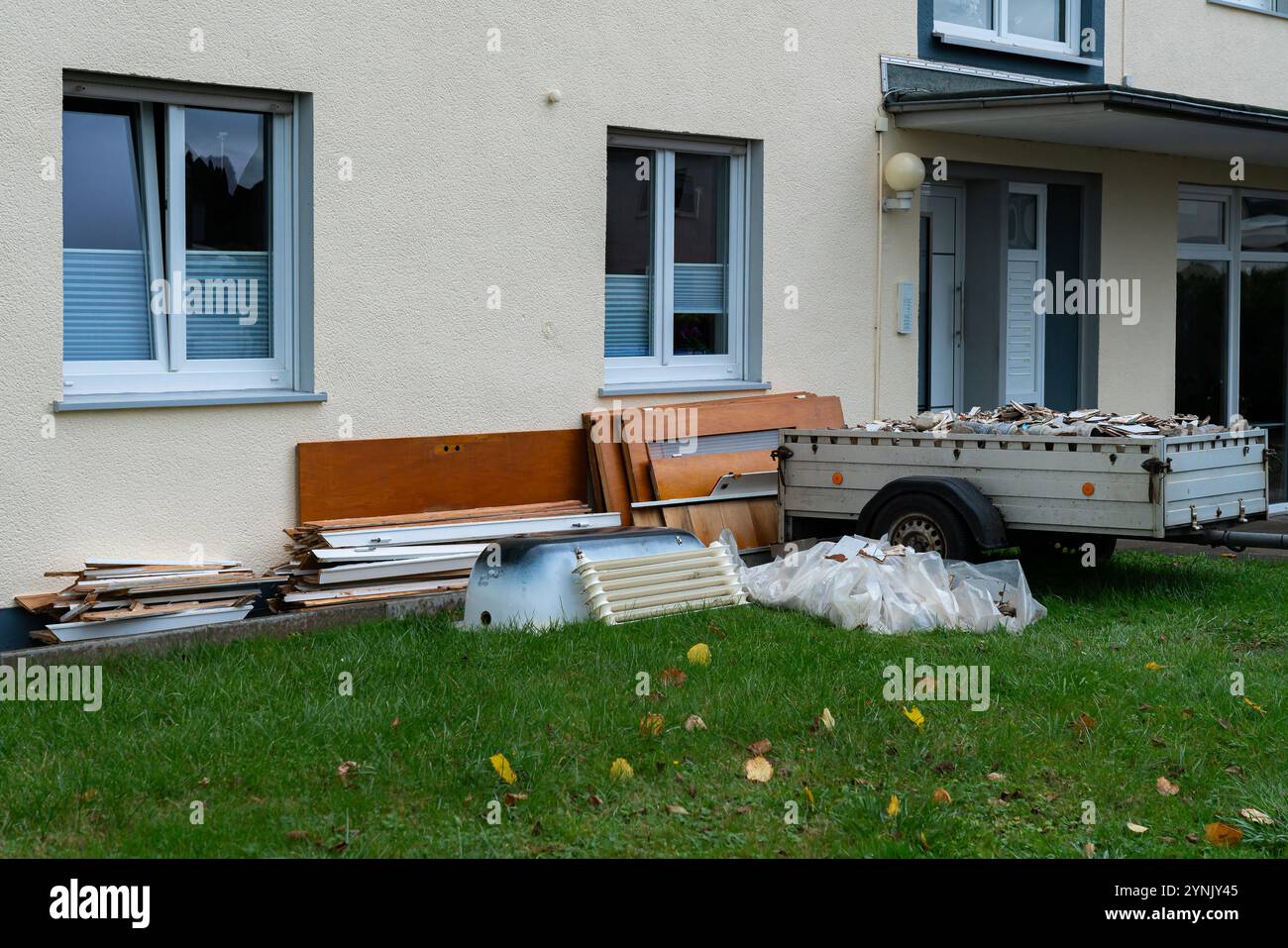 Vari materiali da costruzione e detriti sono accumulati all'esterno di un edificio residenziale su un'area erbosa, mostrando un ambiente poco ordinato con i gettati Foto Stock