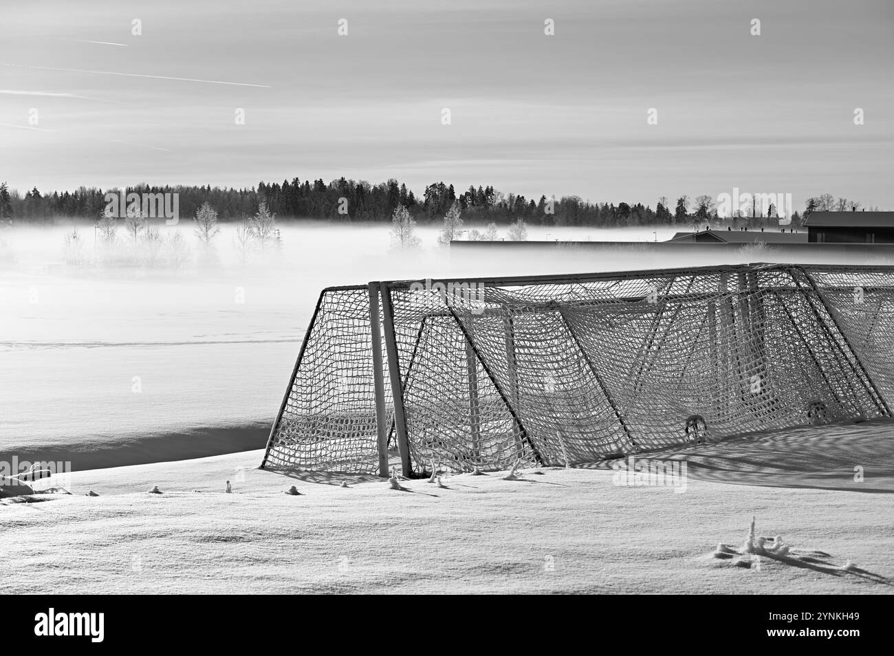 la fotografia in bianco e nero cattura un tranquillo paesaggio invernale con una porta di calcio smerigliata su un campo innevato. La nebbia si avvolge delicatamente sulla parte anteriore Foto Stock