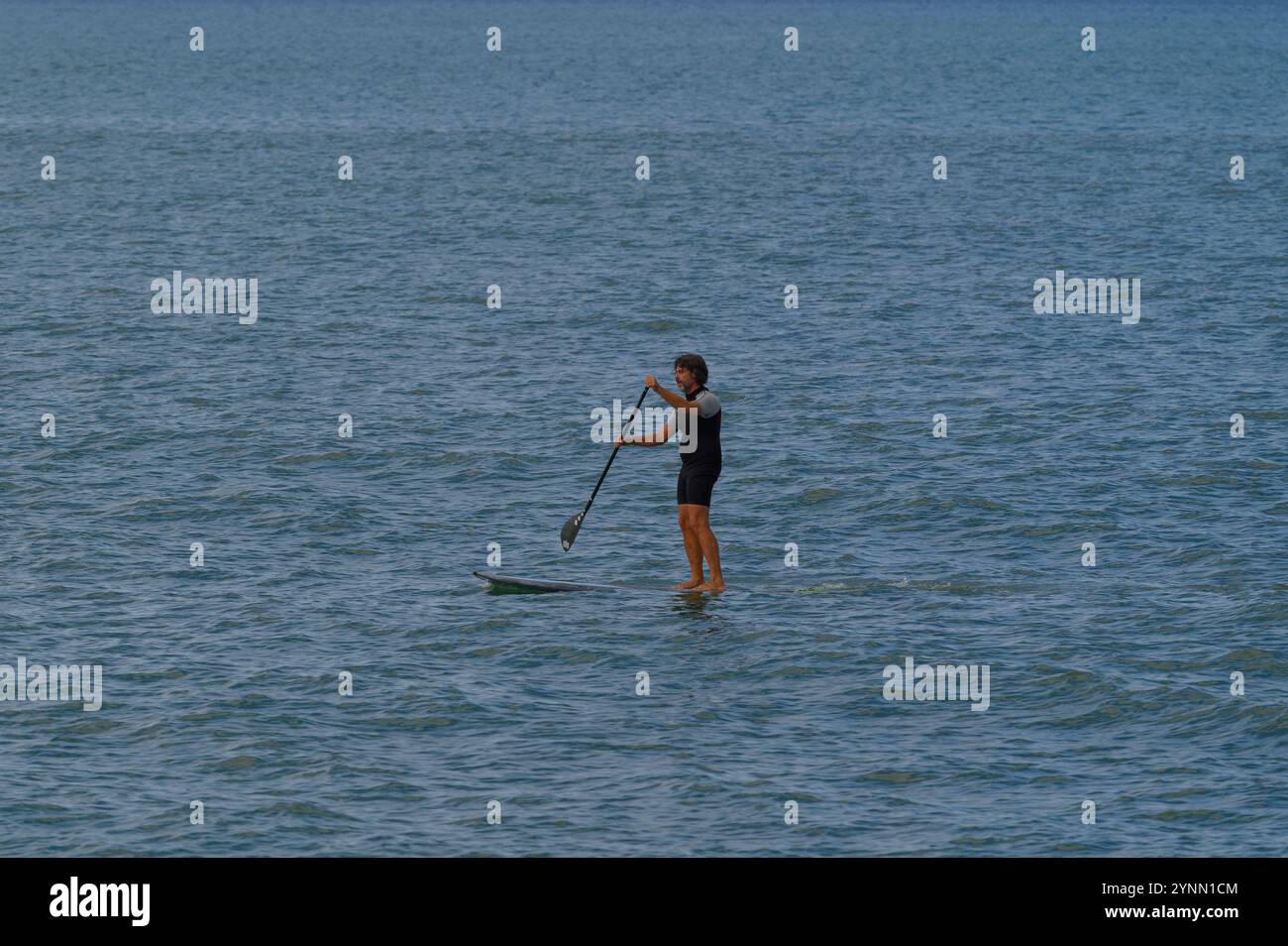 Una pedalata solitaria scivola attraverso le calme acque del Mar Mediterraneo, godendosi una giornata tranquilla e soleggiata, Toscana, Italia Foto Stock