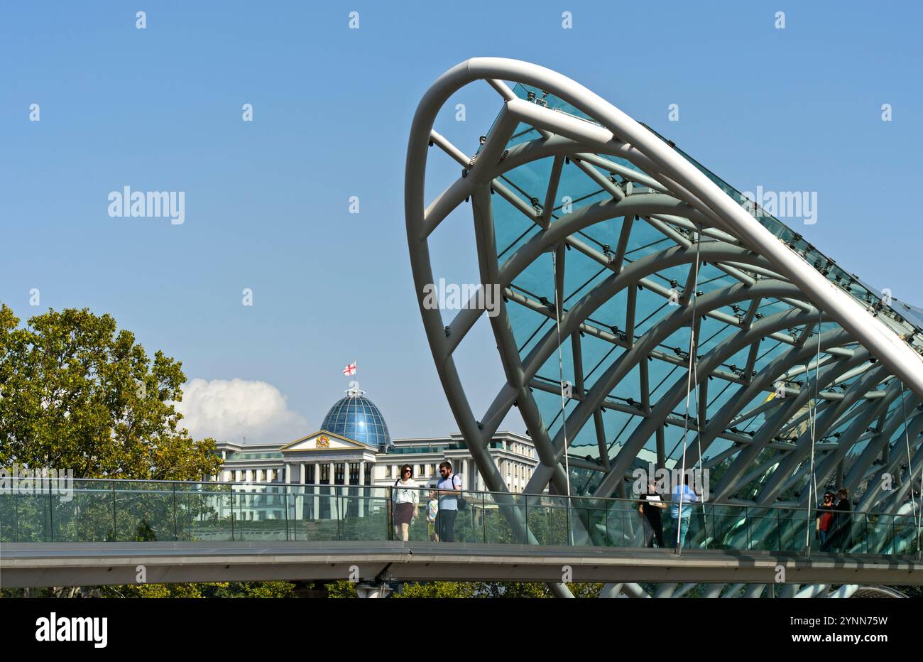 Futuristico Peace Bridge a forma di arco sul fiume Kura, dietro il Palazzo dei Festival della Georgia, ex Palazzo Presidenziale, Tbilisi, Georgia Foto Stock
