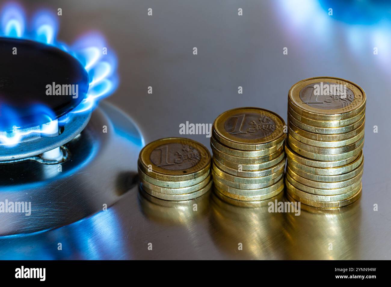 Fornello a gas illuminato, con pile di monete sopra di esso. Aumento dei costi e delle tariffe del gas. Foto Stock