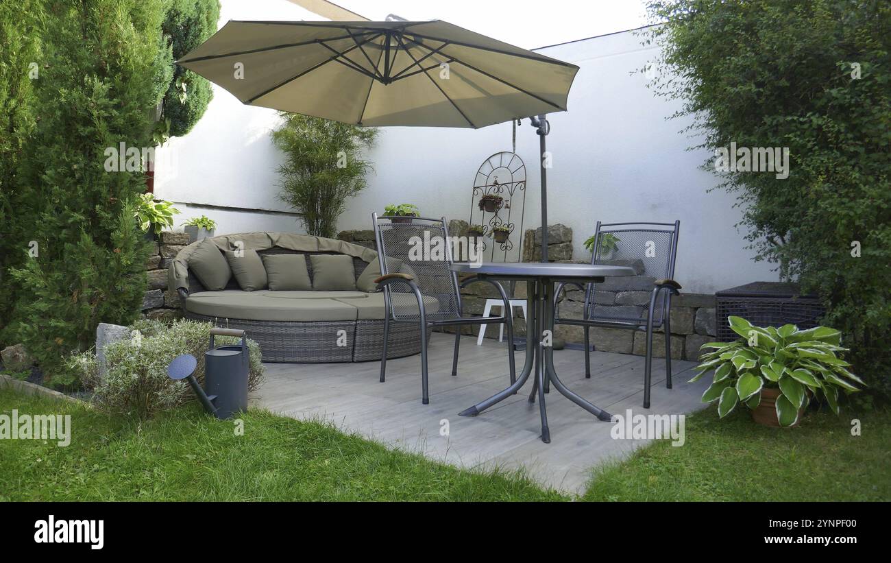 Terrazza giardino con salotto e area salotto e ombrellone in un angolo del giardino con un albero di pino colonnare u Foto Stock