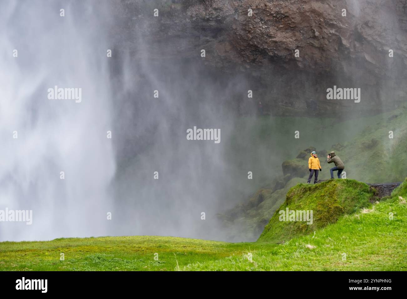 Fotografo turistico che cattura il paesaggio mozzafiato delle cascate islandesi in un giorno nuvoloso - autentica avventura di viaggio nella natura nordica Foto Stock