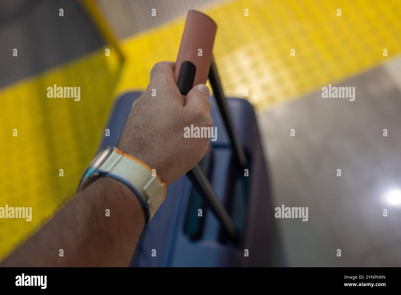 Primo piano di un viaggiatore che tiene una maniglia per valigia vicino alla pavimentazione tattile Foto Stock