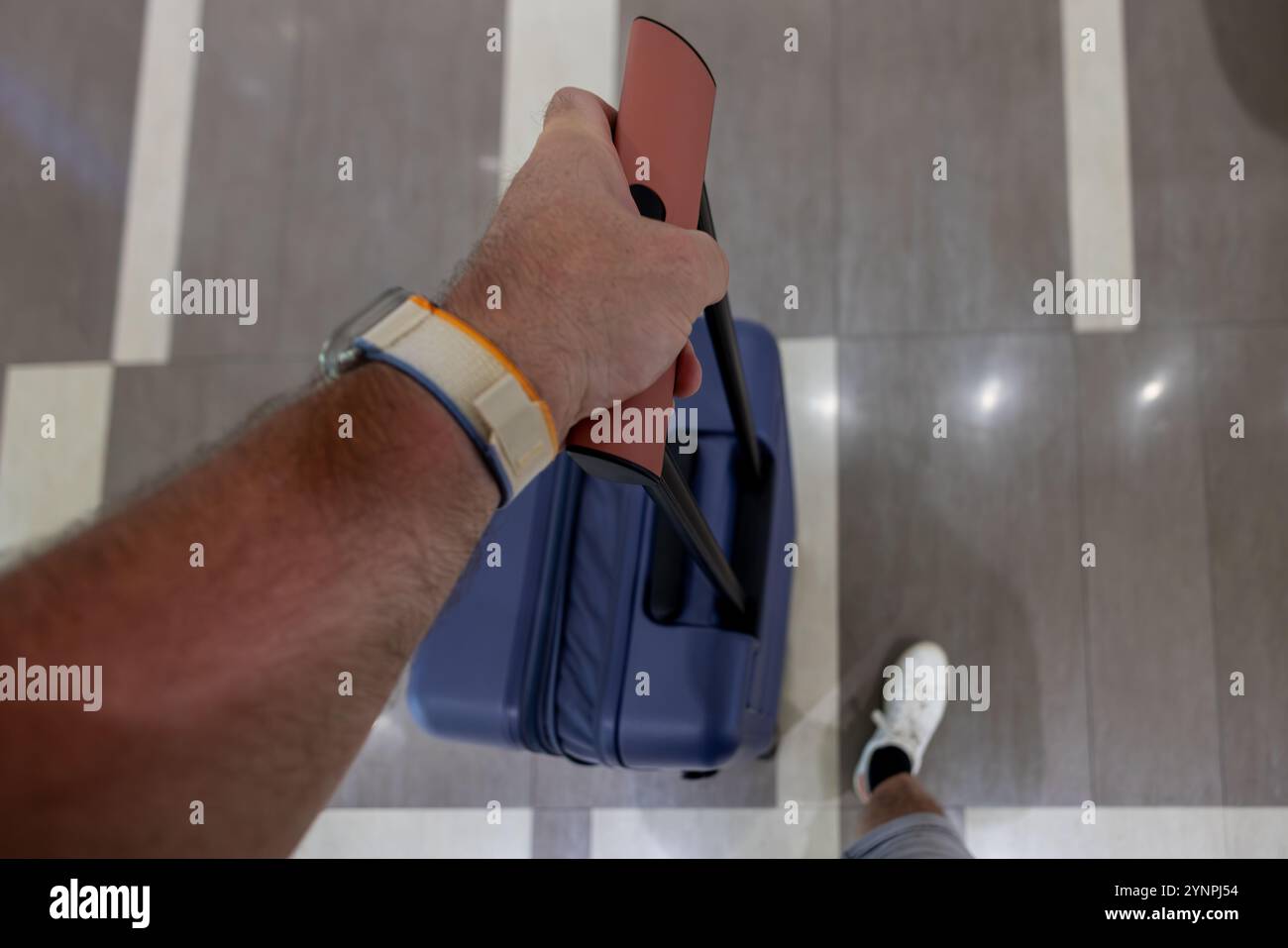 Viaggiatore che tiene la maniglia di una valigia in un terminal dell'aeroporto Foto Stock