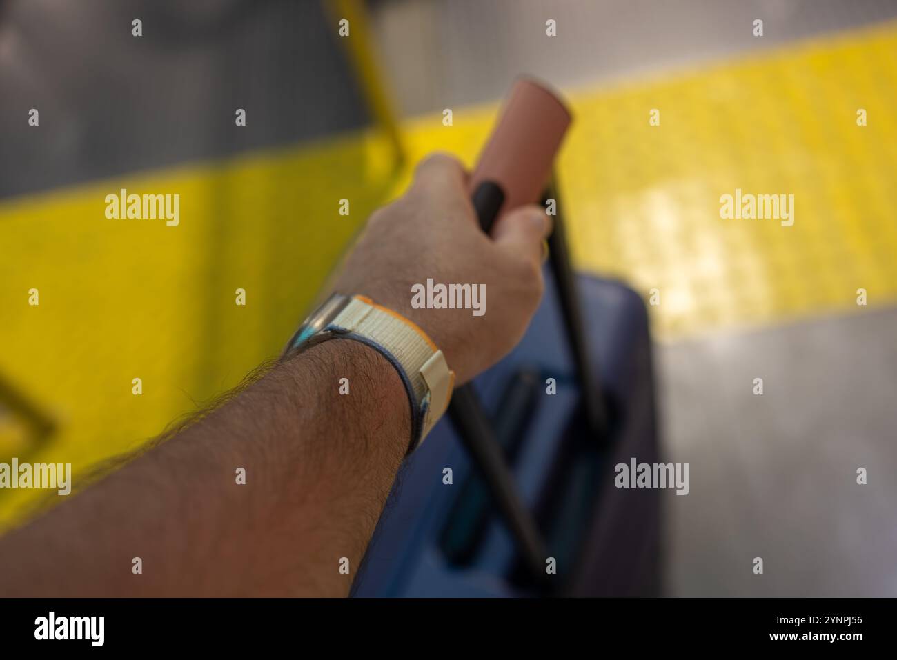 Viaggiatore che tiene una maniglia per valigia vicino a una piattaforma con pavimentazione tattile gialla Foto Stock