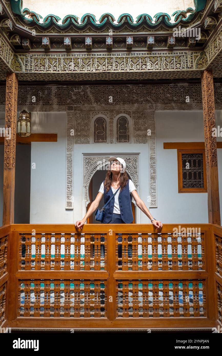 Giovane donna dai capelli scuri appoggiata su ringhiere di legno nel cortile della Madrasa di Ben Youssef, Marocco Foto Stock