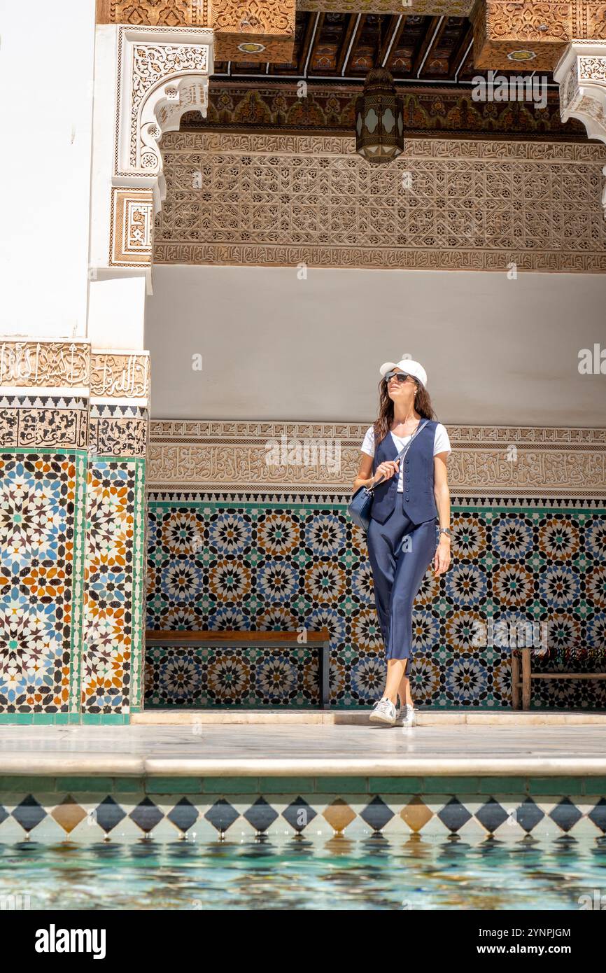 Giovane donna dai capelli scuri in pantaloni blu navy camicia bianca e berretto nel cortile della Madrasa Ben Youssef, Marocco Foto Stock