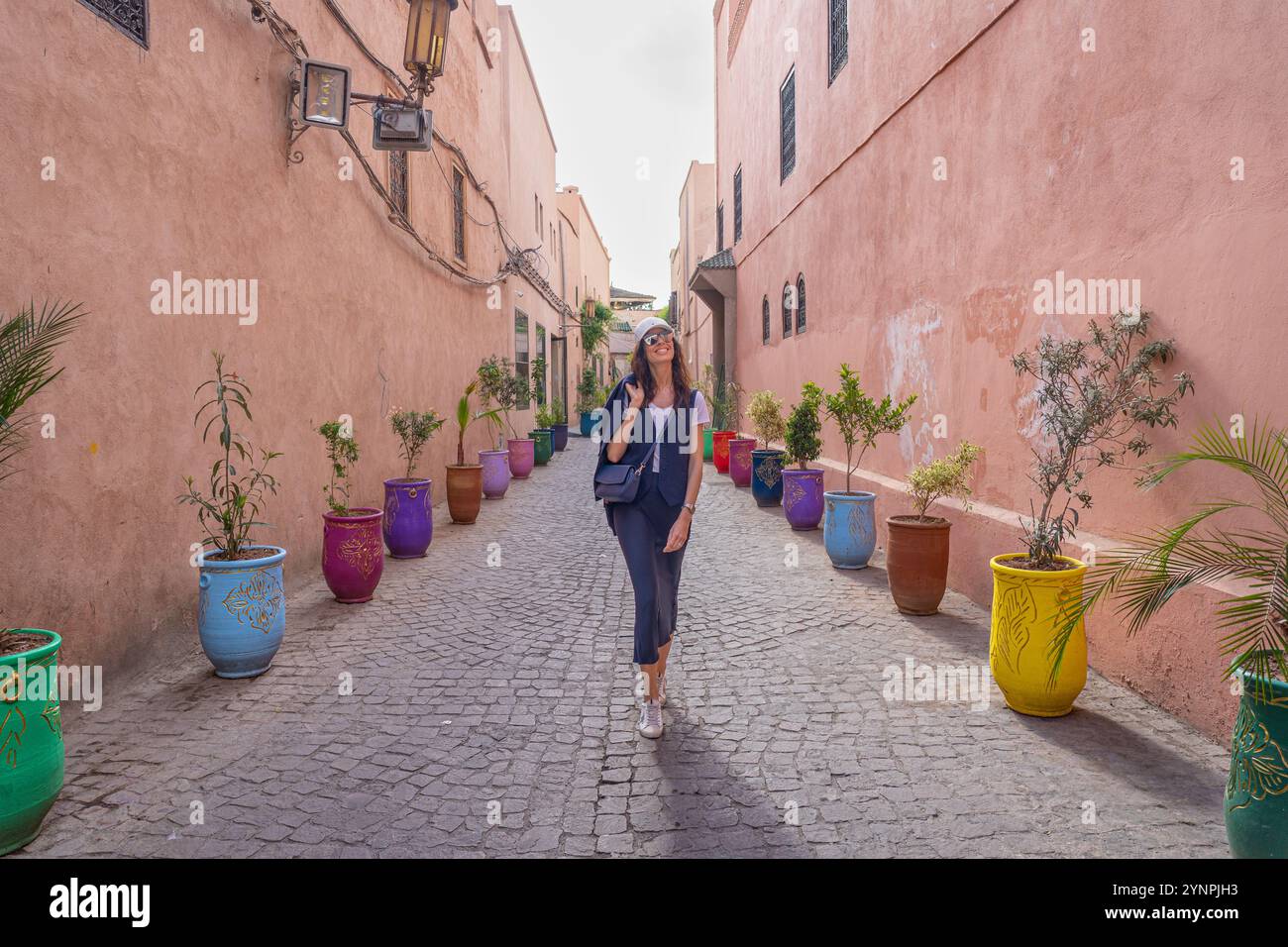 Giovane donna dai capelli scuri che cammina nelle strade rosse di Marrakech circondata da vasi colorati, il Marocco Foto Stock