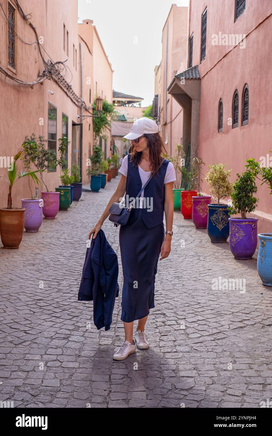 Giovane donna dai capelli scuri che cammina nelle strade rosse di Marrakech circondata da vasi colorati, il Marocco Foto Stock