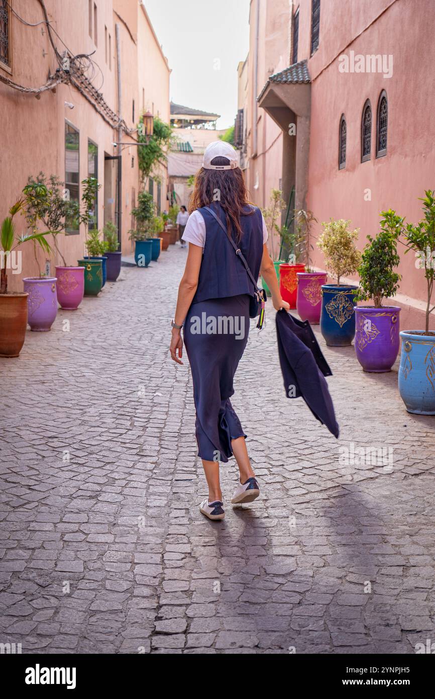 Giovane donna dai capelli scuri che cammina nelle strade rosse di Marrakech circondata da vasi colorati, il Marocco Foto Stock