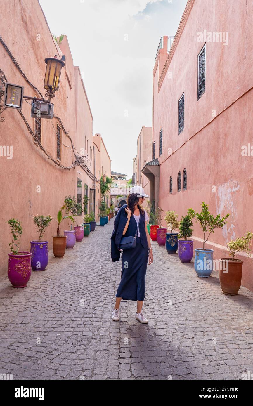 Giovane donna dai capelli scuri che cammina nelle strade rosse di Marrakech circondata da vasi colorati, il Marocco Foto Stock