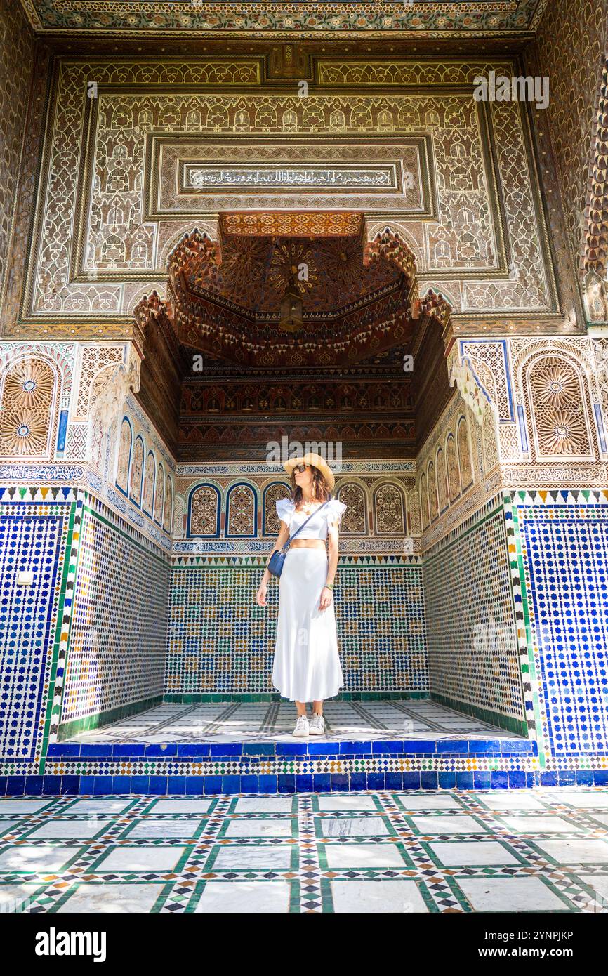 Giovane donna dai capelli scuri in camicia bianca con cappello e gonna in posa nel cortile del Palazzo Bahia di Marrakech, Marocco Foto Stock