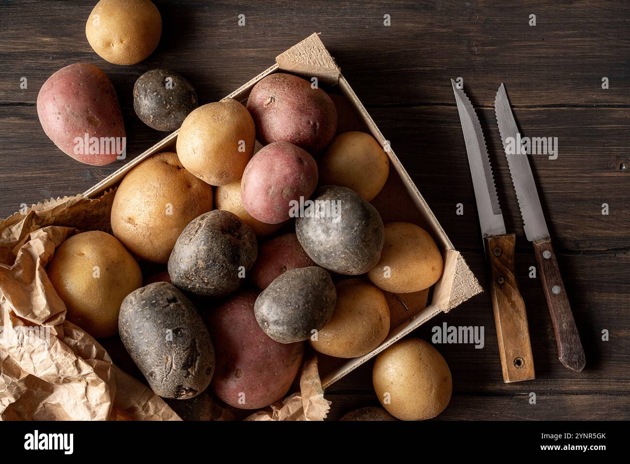 Gruppo di diversi tipi di patate: Patate viola, patate rosse e patate russate, su un tavolo di legno scuro. Foto Stock