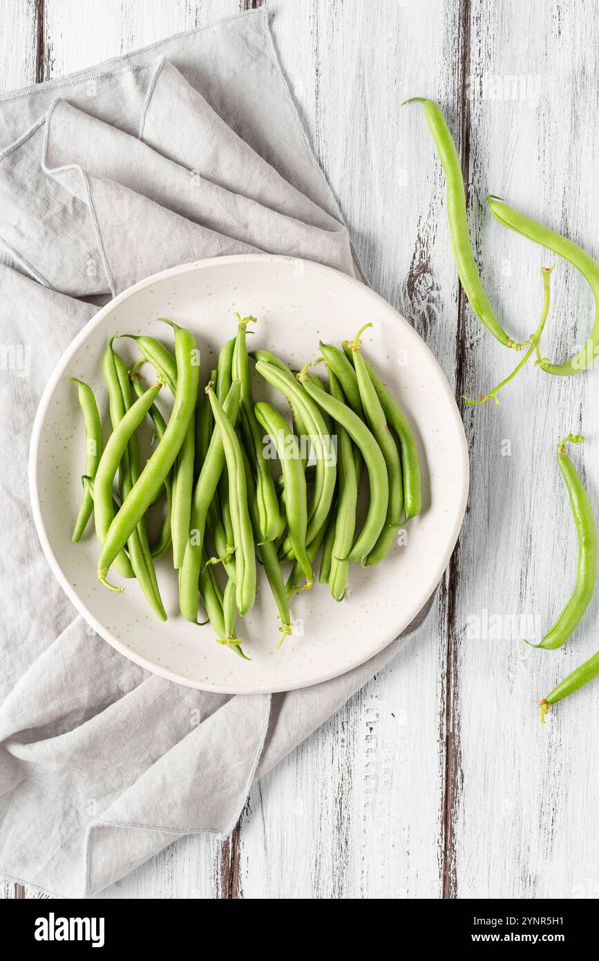 Fagioli verdi appena raccolti, in un piatto, su un tavolo di legno bianco. Vista dall'alto. Foto Stock