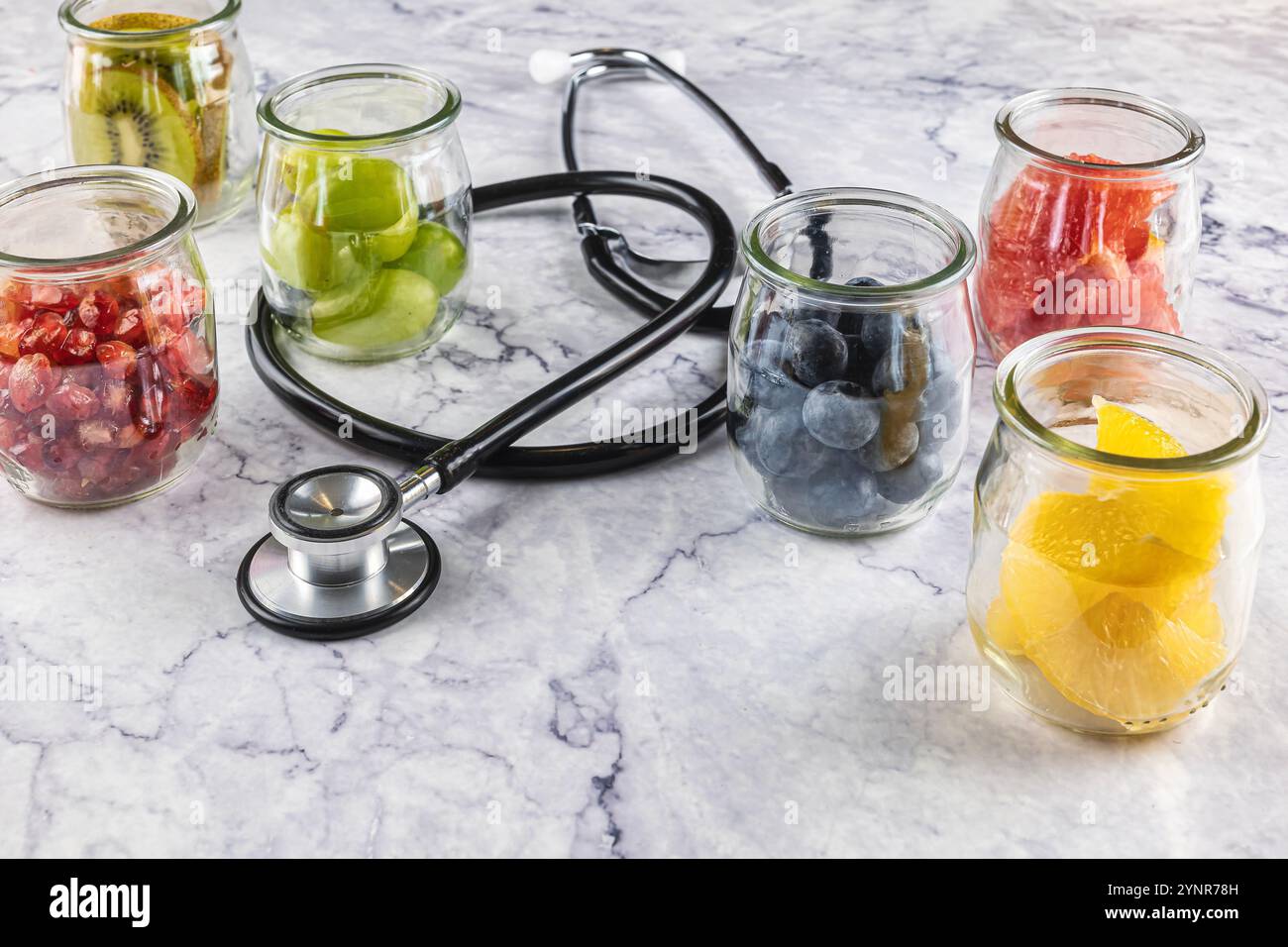 Vasi di frutta con kiwi, melograno, uva, arancia, pompelmo, mirtillo e banana. Cibo contro le malattie e il cancro. Uno stetoscopio al centro di t Foto Stock