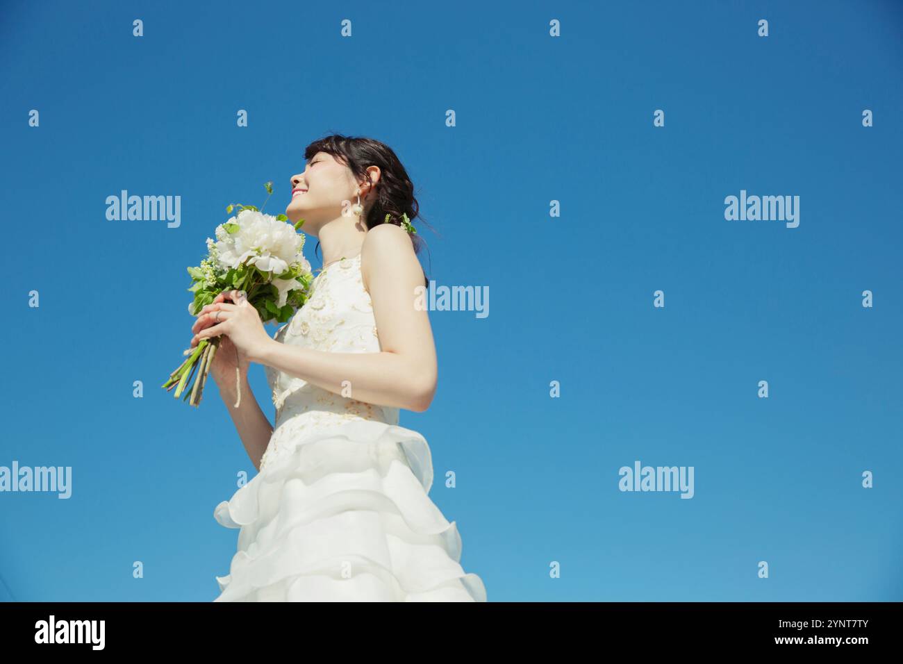 Donna sui vent'anni in abito da sposa in piedi sotto il cielo blu Foto Stock
