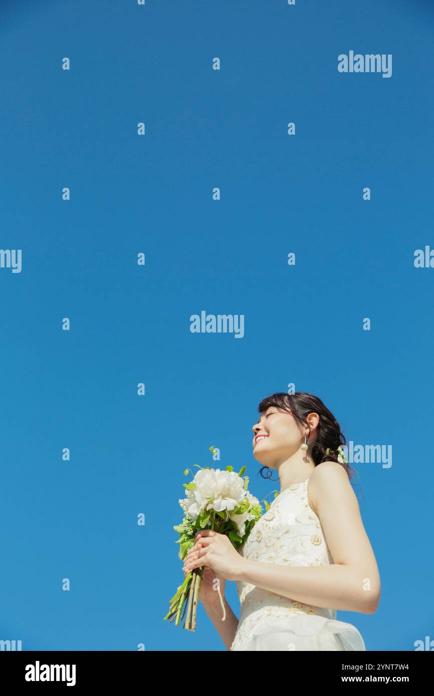 Donna sui vent'anni in abito da sposa in piedi sotto il cielo blu Foto Stock
