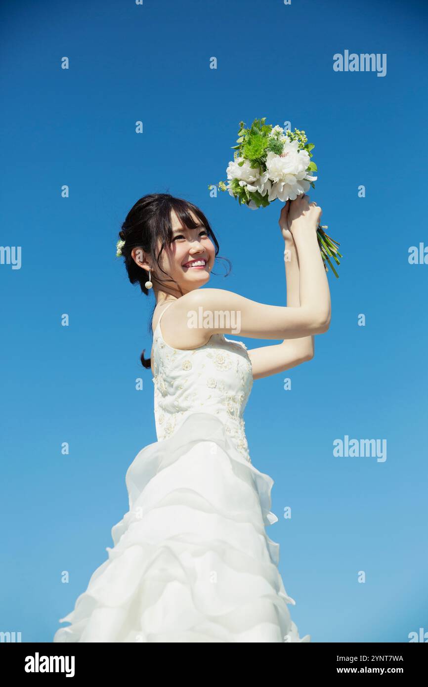 Donna sui vent'anni in abito da sposa in piedi sotto il cielo blu Foto Stock