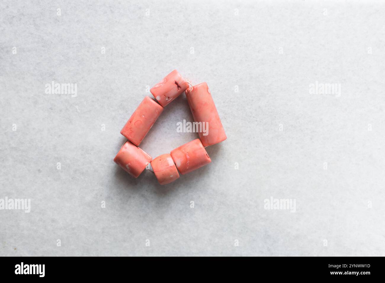 Vista dall'alto di autentiche perle di corallo rosa su un vassoio di marmo, vista dall'alto di grandi perle di corallo rosa a corde su un tavolo bianco Foto Stock