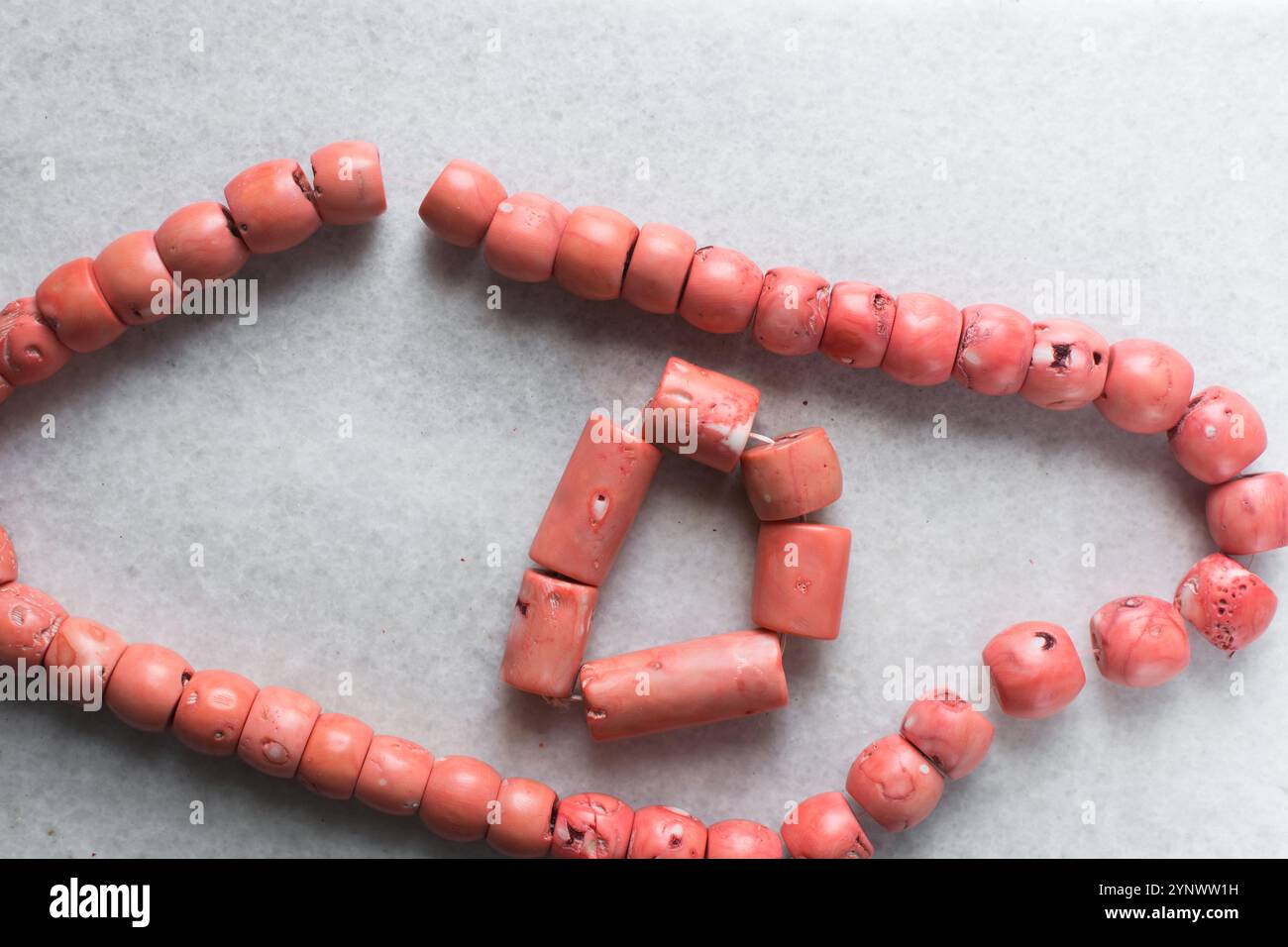 Vista dall'alto di autentiche perle di corallo rosa su un vassoio di marmo, vista dall'alto di grandi perle di corallo rosa a corde su un tavolo bianco Foto Stock