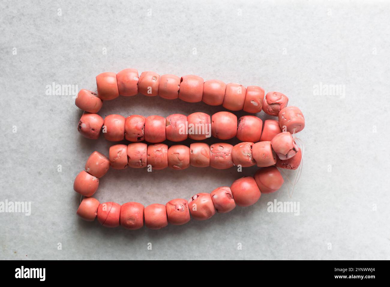 Vista dall'alto di autentiche perle di corallo rosa su un vassoio di marmo, vista dall'alto di grandi perle di corallo rosa a corde su un tavolo bianco Foto Stock