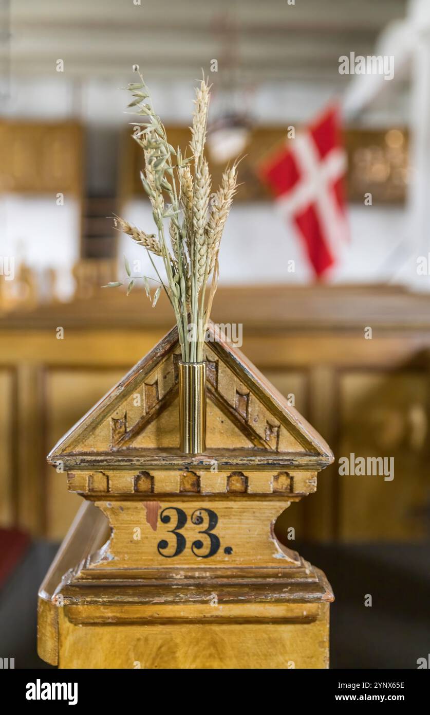 Un dettaglio rustico in legno con un vaso di grano all'interno. La bandiera danese e l'ambientazione della chiesa suggeriscono temi culturali e storici Foto Stock Un dettaglio rustico in legno con un vaso di grano all'interno. La bandiera danese e l'ambientazione della chiesa suggeriscono temi culturali e storici Foto Stock