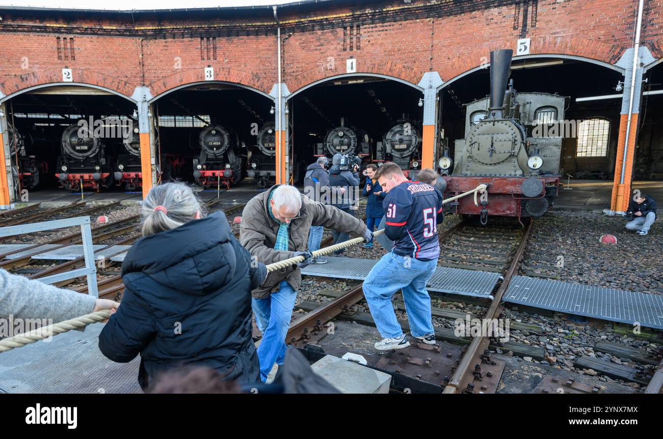 27 novembre 2024, Sassonia, Chemnitz: Con forze combinate, gli ospiti del Museo ferroviario sassone di Chemnitz tirano fuori dal capannone la locomotiva a vapore "Hegel" (98 7056), che pesa oltre 20 tonnellate. La locomotiva, costruita nel 1886 presso la Sächsische Maschinenfabrik, ex Richard Hartmann AG, è una delle mostre ed è stata ora estratta dal capannone da volontari su base di test. Per la cerimonia di apertura dell'anno della capitale della cultura, un totale di dieci squadre di 12 persone sono state ricercate per tirare la locomotiva normalmente da 250 cv a una certa distanza in una competizione. Questo evento fa parte Foto Stock