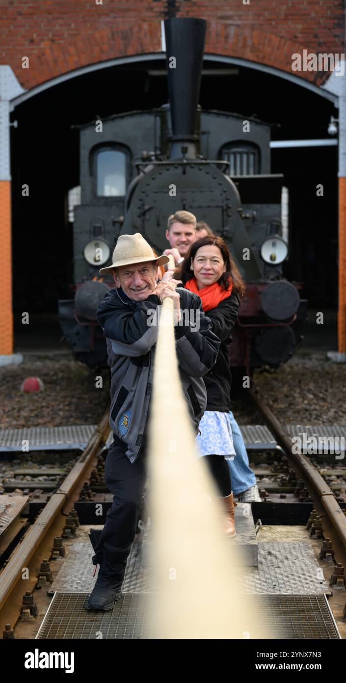 27 novembre 2024, Sassonia, Chemnitz: Con forze combinate, gli ospiti del Museo ferroviario sassone di Chemnitz tirano fuori dal capannone la locomotiva a vapore "Hegel" (98 7056), che pesa oltre 20 tonnellate. La locomotiva, costruita nel 1886 presso la Sächsische Maschinenfabrik, ex Richard Hartmann AG, è una delle mostre ed è stata ora estratta dal capannone da volontari su base di test. Per la cerimonia di apertura dell'anno della capitale della cultura, un totale di dieci squadre di 12 persone sono state ricercate per tirare la locomotiva normalmente da 250 cv a una certa distanza in una competizione. Questo evento fa parte Foto Stock