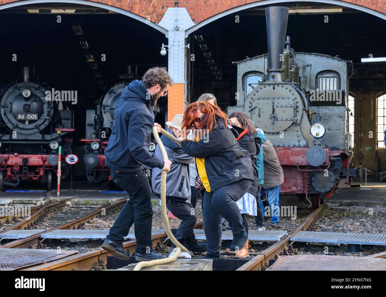 27 novembre 2024, Sassonia, Chemnitz: Con forze combinate, gli ospiti del Museo ferroviario sassone di Chemnitz tirano fuori dal capannone la locomotiva a vapore "Hegel" (98 7056), che pesa oltre 20 tonnellate. La locomotiva, costruita nel 1886 presso la Sächsische Maschinenfabrik, ex Richard Hartmann AG, è una delle mostre ed è stata ora estratta dal capannone da volontari su base di test. Per la cerimonia di apertura dell'anno della capitale della cultura, un totale di dieci squadre di 12 persone sono state ricercate per tirare la locomotiva normalmente da 250 cv a una certa distanza in una competizione. Questo evento fa parte Foto Stock