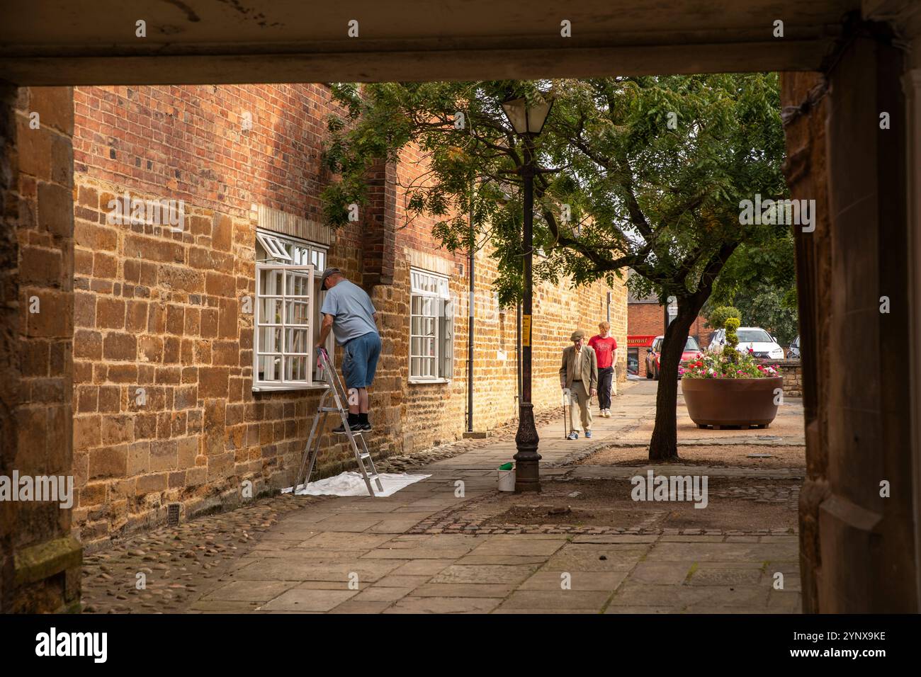 Regno Unito, Inghilterra, Rutland, Uppingham, High Street East, Mercer's Yard to North Street Car Park, uomo che dipinge la finestra Foto Stock