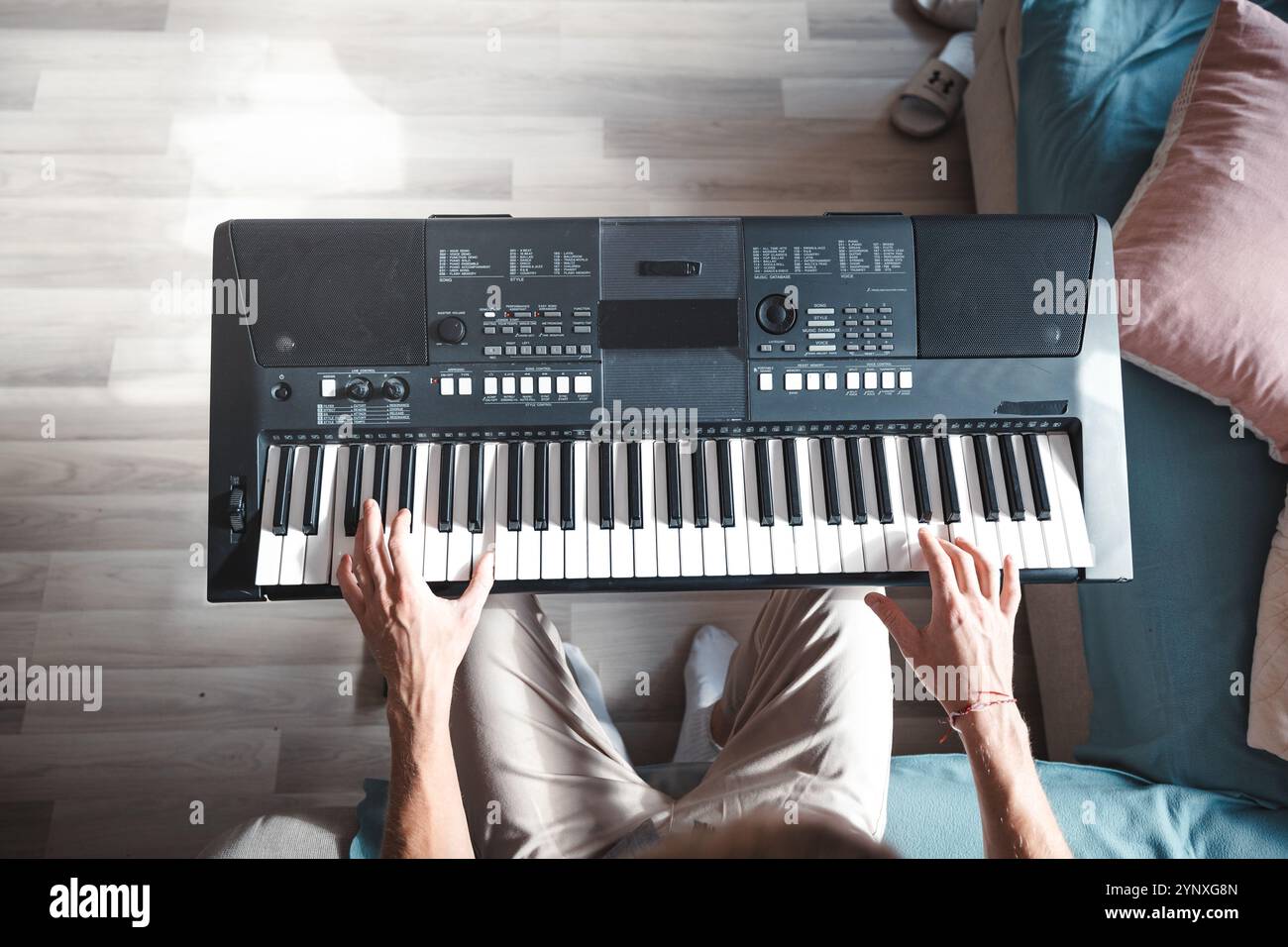 Primo piano di mani che suona una tastiera digitale sotto una calda luce naturale, catturando l'essenza della creatività, della concentrazione e della passione musicale in un ambiente intimo Foto Stock