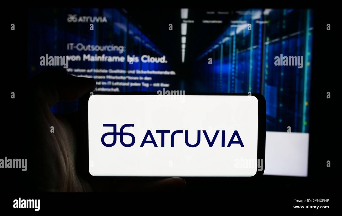 In questa immagine, una persona ha in mano uno smartphone con il logo dell'azienda tedesca di tecnologia dell'informazione Atruvia AG davanti alla pagina Web aziendale. Foto Stock