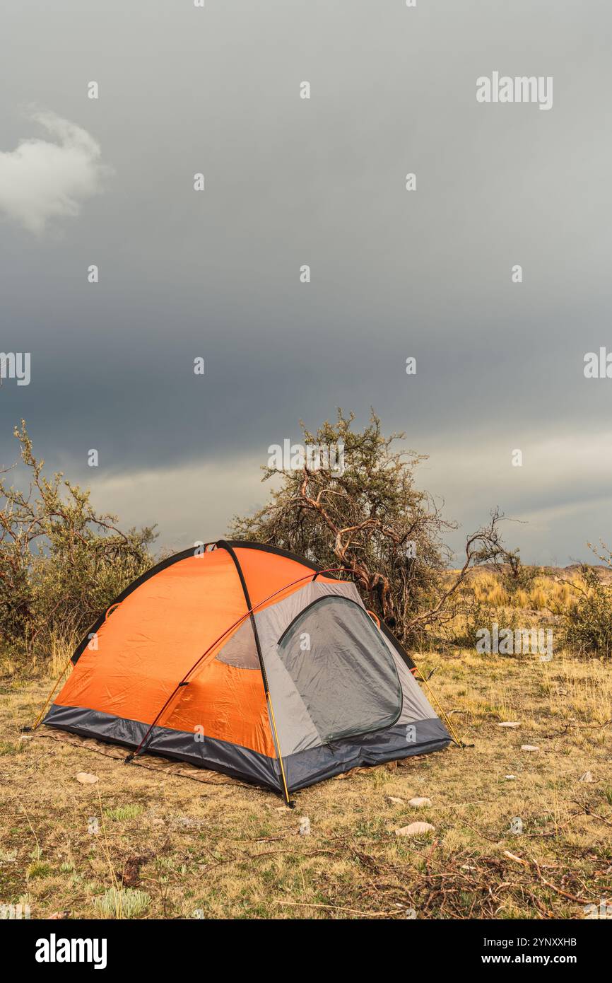 tenda delle highland arancioni nella catena montuosa delle ande circondata da nuvole di tempesta e alberi Foto Stock