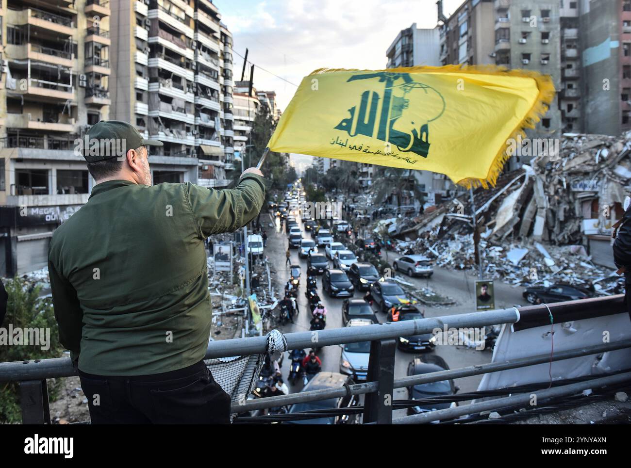 Beirut, Libano. 27 novembre 2024. L'uomo ha issato la bandiera Hezbollah, come cittadini libanesi, con striscioni, restituisce le loro case con veicoli dopo che l'accordo di cessate il fuoco tra Israele e Libano è entrato in vigore nella regione Dahieh di Beirut, Libano, il 27 novembre 2024. Foto di FADEL ITANI/UPI. Crediti: UPI/Alamy Live News Foto Stock