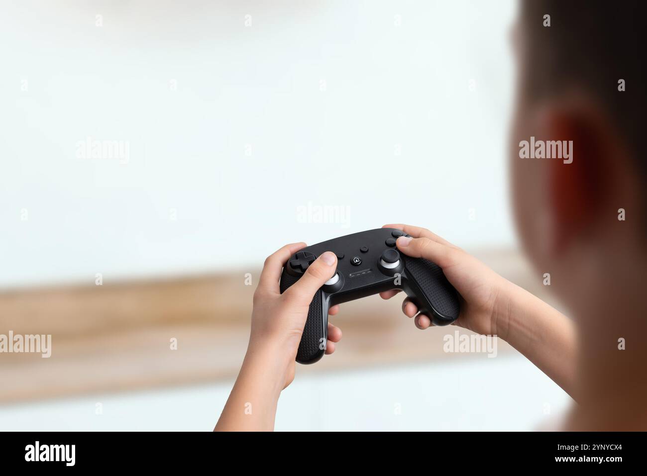 Vista a spalla di un ragazzo che regge un gamepad, sfondo pulito con spazio vuoto per il testo, perfetto per promozioni di gioco e pubblicità creativa Foto Stock