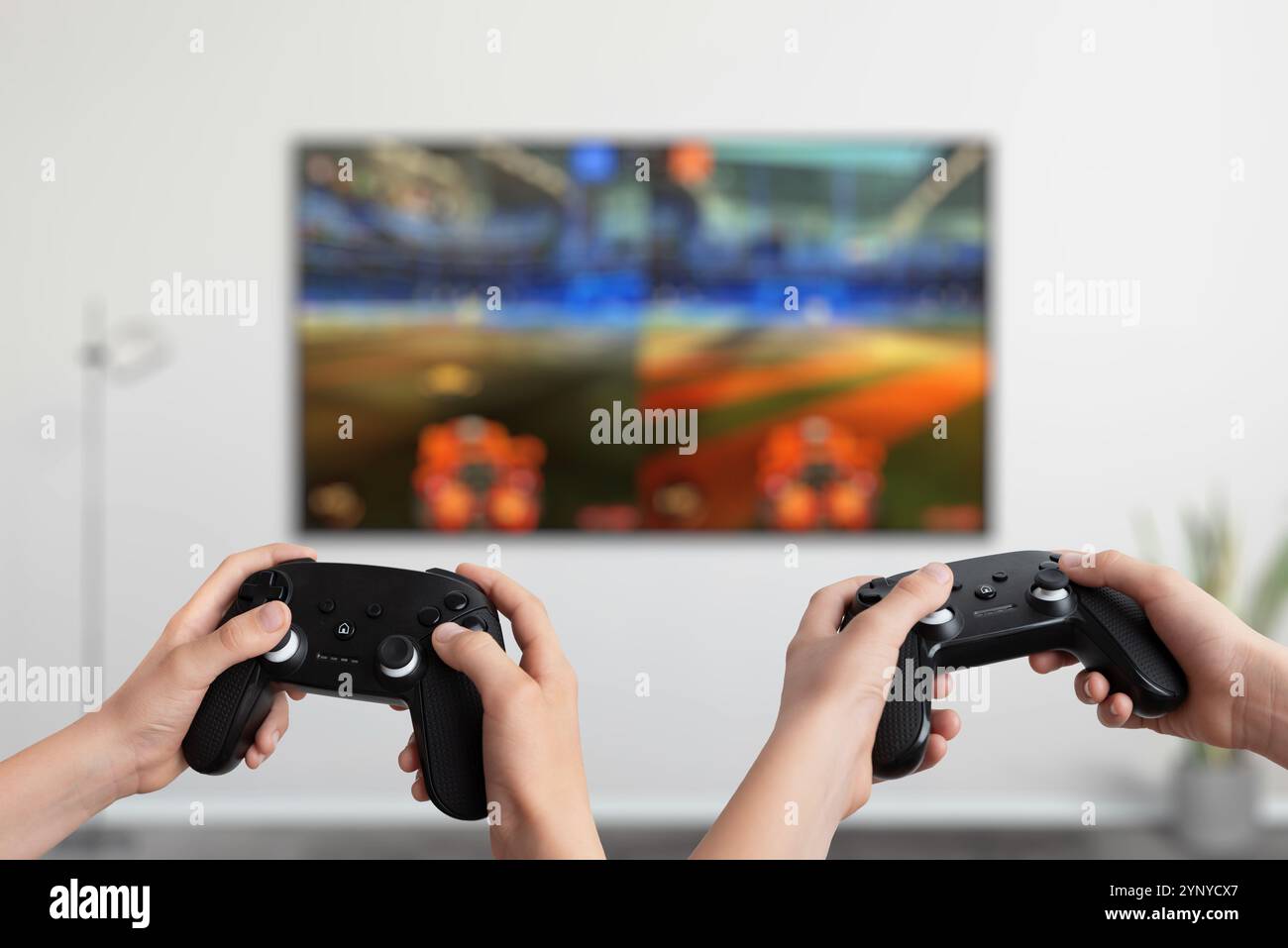 Due giocatori che tengono i gamepad davanti a una TV e giocano a un gioco d'azione a schermo diviso, che mette in mostra giochi multigiocatore interattivi e intrattenimento dinamico Foto Stock