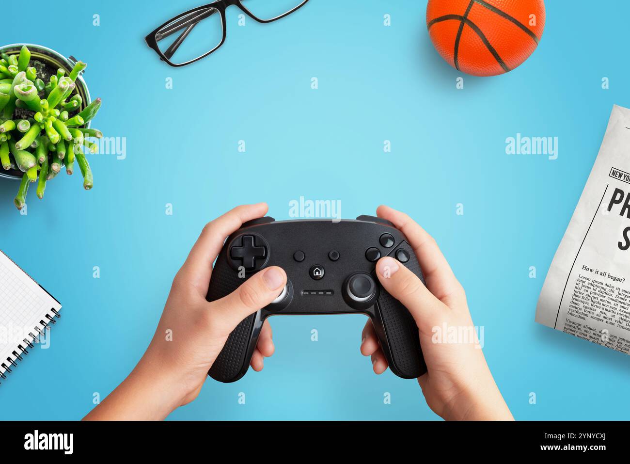 Vista dall'alto composizione piatta di un giocatore che tiene un gamepad su una scrivania con palla, giornale, occhiali, pianta e blocco note, perfetto per i videogame creativi Foto Stock