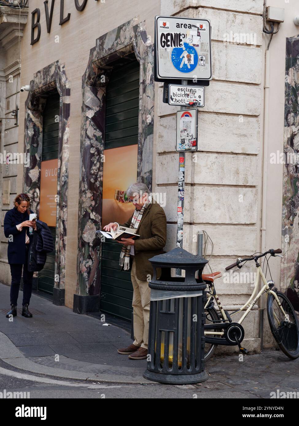 Un uomo maturo ben vestito con gli occhiali legge un libro su un angolo di strada accanto a un bidone della spazzatura e a una bicicletta a Roma, in Italia. 27 novembre 2024 Foto Stock Un uomo maturo ben vestito con gli occhiali legge un libro su un angolo di strada accanto a un bidone della spazzatura e a una bicicletta a Roma, in Italia. 27 novembre 2024 Foto Stock