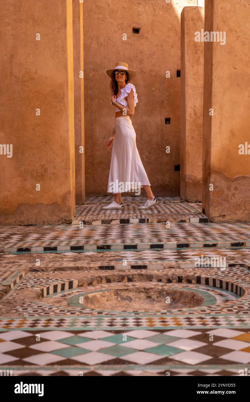 Giovane donna dai capelli scuri in abito bianco e cappello in posa al Palazzo El Badii di Marrakech con piastrelle colorate, Marrakech Foto Stock