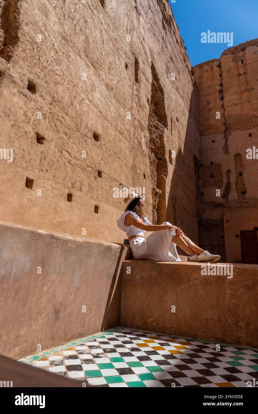 Giovane donna dai capelli scuri in abito bianco e cappello in posa al Palazzo El Badii di Marrakech con piastrelle colorate, Marrakech Foto Stock