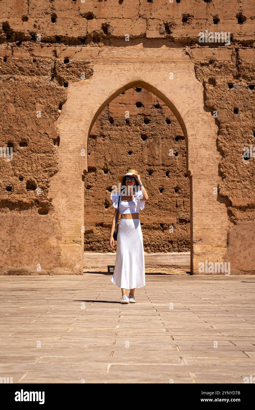 Giovane donna dai capelli scuri con abito bianco e cappello in posa nel cortile esterno del Palazzo El Badii di Marrakech, Marocco Foto Stock