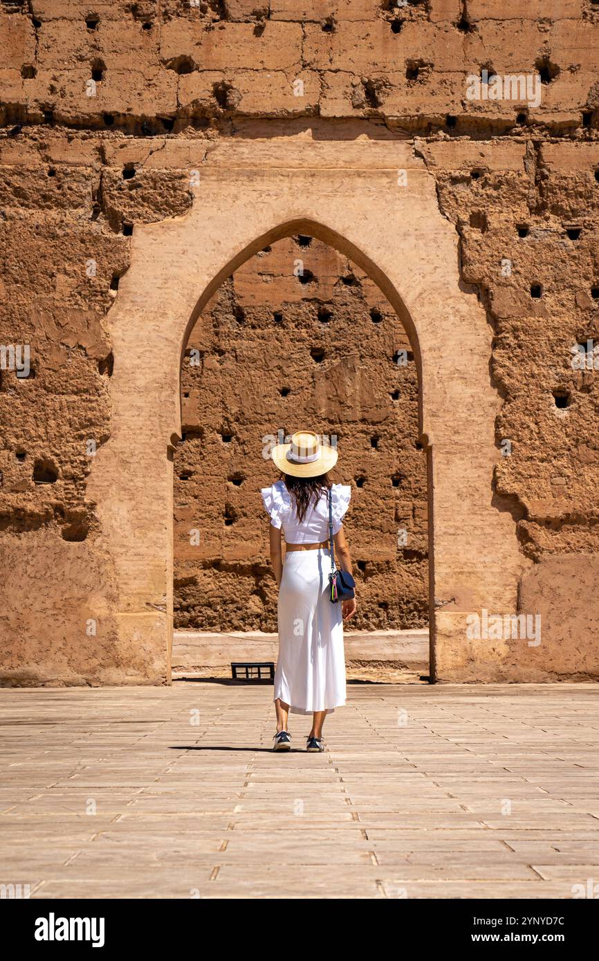 Giovane donna dai capelli scuri con abito bianco e cappello in posa nel cortile esterno del Palazzo El Badii di Marrakech, Marocco Foto Stock
