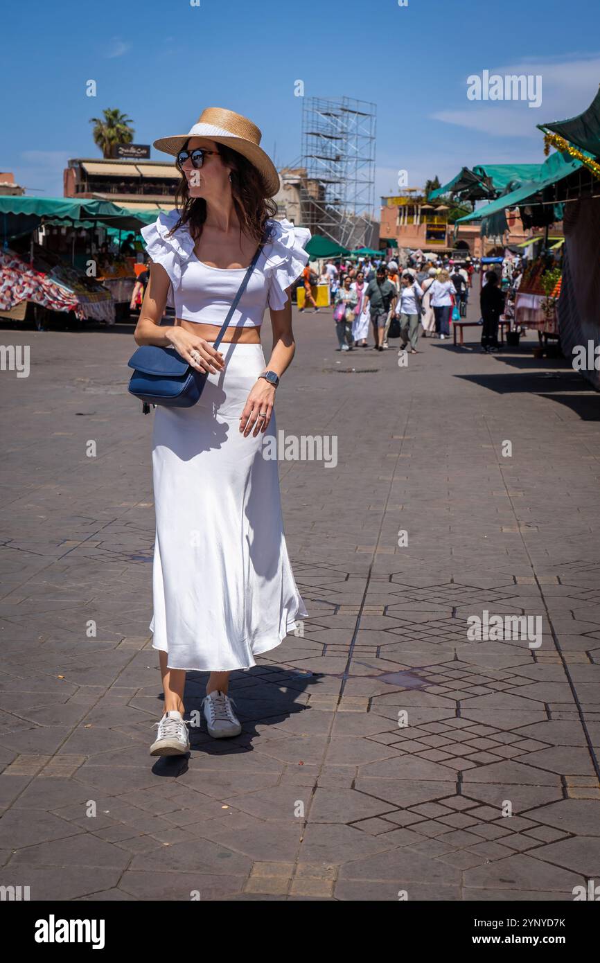 Giovane donna dai capelli scuri in abito bianco e cappello in posa durante il giorno in Piazza Jama El Fnaa, Marocco Foto Stock